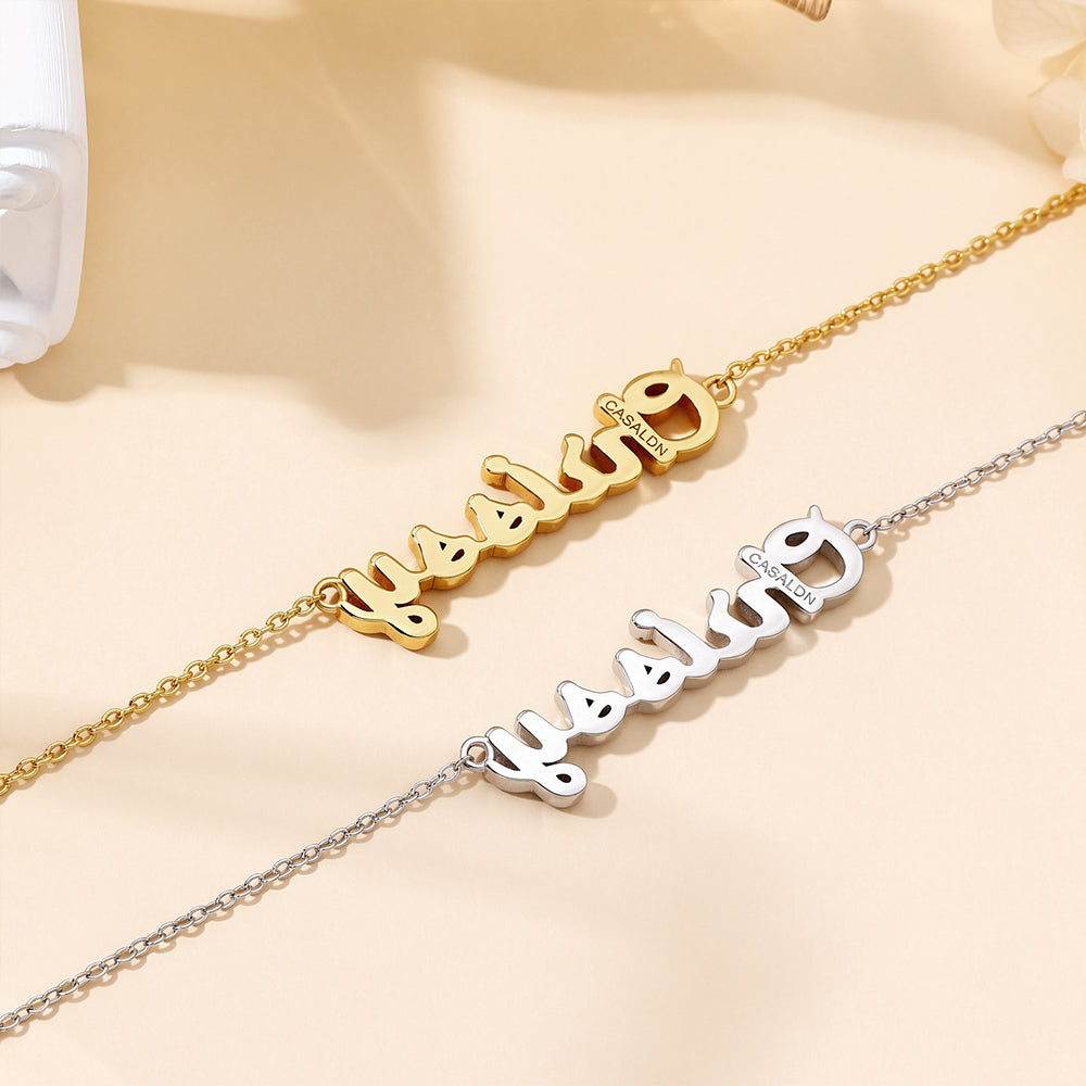 Flat lay of two CASA London Custom Pavé Name Necklaces side by side on a cream background — one in 18ct gold vermeil and one in rhodium silver on S925 sterling silver — both displaying the engraved CASA London brand insignia on the pendant