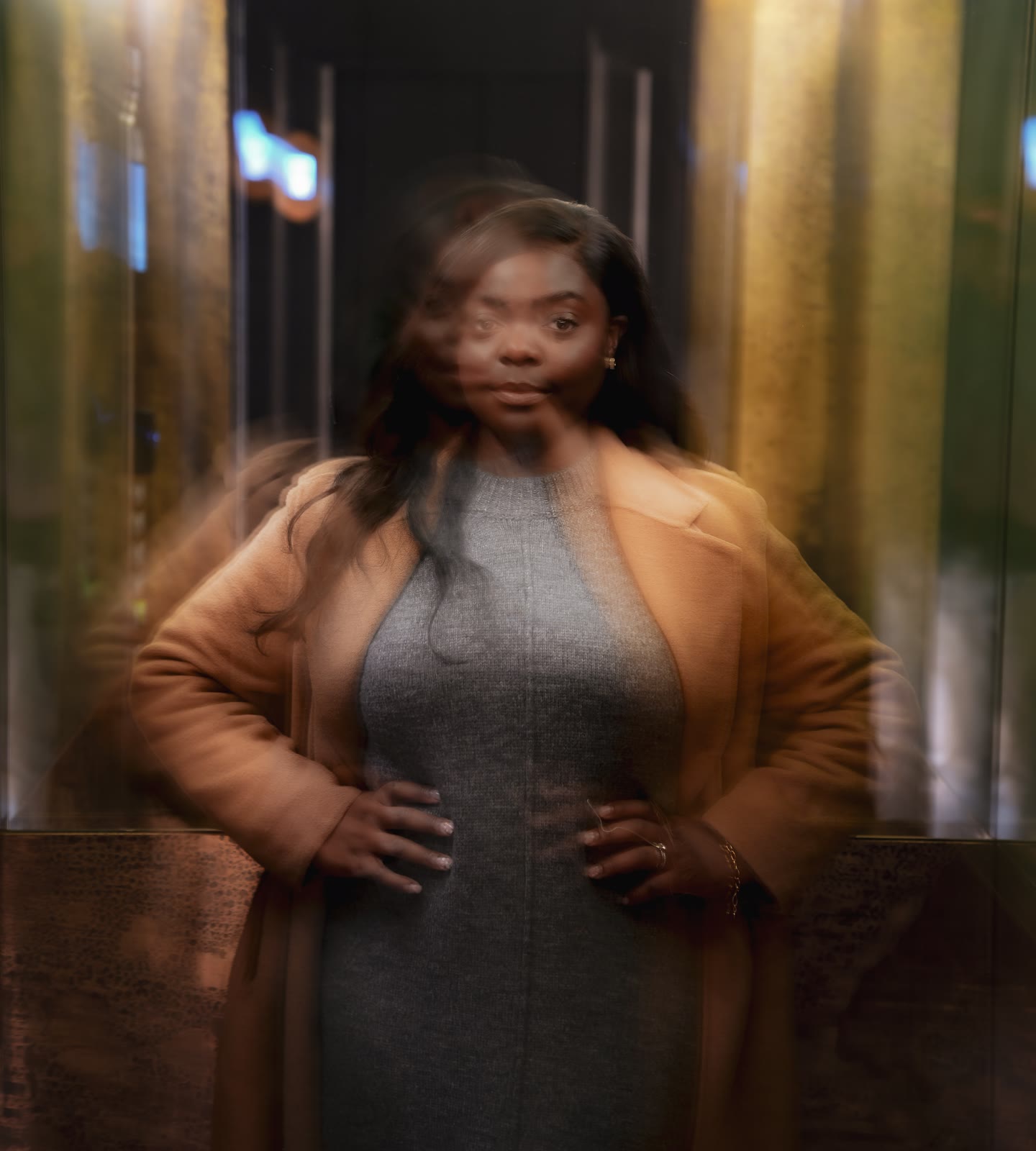 Soft motion-blur portrait of Christine, founder of CASA London, with her hands on her hips in a camel coat inside a gold-lit lift