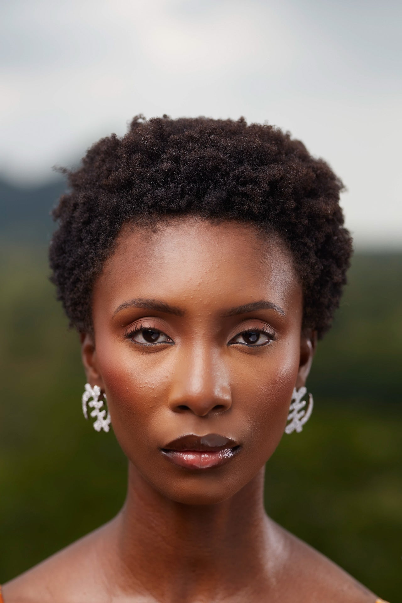 Model wearing large silver Gye Nyame Adinkra symbol earrings set with high-grade zircon stones, showcasing the traditional Ghanaian symbol of 'Except for God' in a shimmering pavé design.