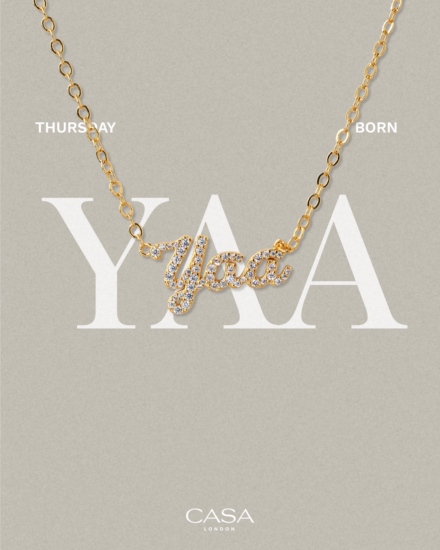 A product shot of CASA London’s gold Yaa Pavé Necklace. The delicate gold chain features a script pendant spelling "Yaa," encrusted with shimmering pavé-set stones against a neutral, textured background. Overlaid text reads "THURSDAY BORN," highlighting the brand's commitment to celebrating cultural heritage and personal narratives through modern luxury.